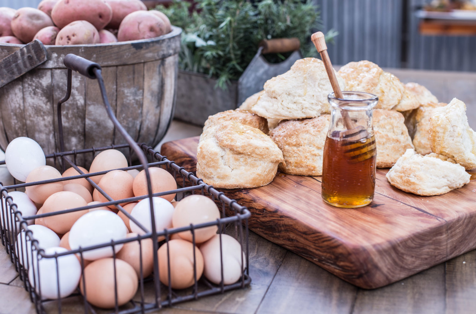biscuits with jar of honey, basket of eggs, and basket of potatoes